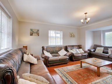A living room with three brown leather sofas a wooden coffee table an orange patterned rug and wall art at Ingleside Adsett Royal Forest of Dean
