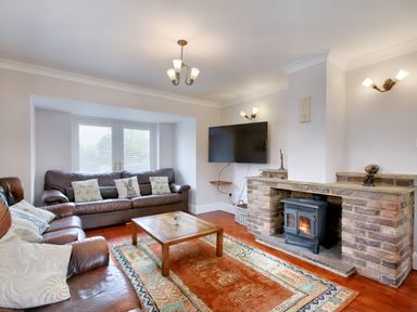 A living room with two brown leather sofas a wooden coffee table a rug fireplace with a wood stove and a wall mounted TV at Ingleside in Adsett Royal Forest of Dean