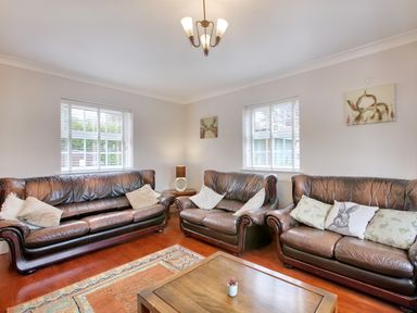 A living room with three brown leather sofas a wooden coffee table with a small plant two windows with white blinds paintings on the walls and a ceiling light at Ingleside in Adsett Royal Forest of Dean