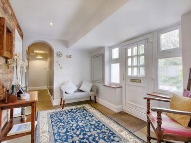 An entry hallway with a blue patterned rug a wooden table a gray cushioned bench a wooden armchair and a white front door at Ingleside Adsett Royal Forest of Dean