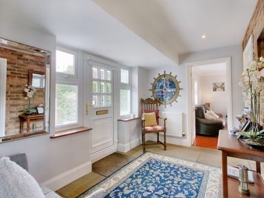 An entryway with white door windows a wooden chair with cushions a blue patterned rug a wooden table with flowers and a large wall mirror at Ingleside Adsett Royal Forest of Dean