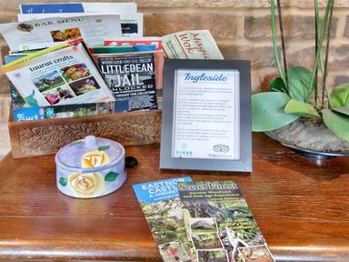 A wooden table with an ornate wooden holder containing leaflets a framed note a ceramic container with a lid and a potted plant at Ingleside Adsett Royal Forest of Dean