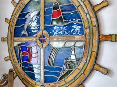 A stained glass artwork shaped like a ship's wheel with images of a dolphin a lighthouse a flag and a rainbow at Ingleside in Adsett Royal Forest of Dean