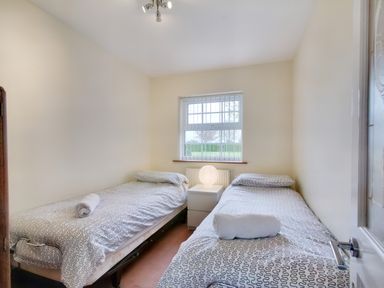 A small bedroom with two single beds a nightstand with a lamp and a window at Ingleside Adsett Royal Forest of Dean