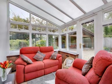 A conservatory with red sofas and patterned cushions overlooking a garden at Ingleside Adsett Royal Forest of Dean