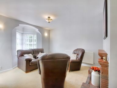 A living room with brown leather chairs a brick fireplace with flowers and a window with white blinds at Ingleside in Adsett Royal Forest of Dean