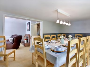 A dining room with a set table and wooden chairs next to a living area with a leather armchair and fireplace at Ingleside in Adsett Royal Forest of Dean