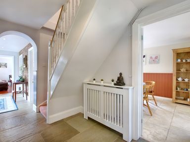 A hallway with staircase radiator cover and small plants next to a dining room with wooden furniture at Ingleside in Adsett Royal Forest of Dean