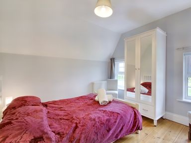 A bedroom with a bed covered with a red patterned bedspread a white wardrobe with mirrored doors and two windows at Ingleside in Adsett Royal Forest of Dean