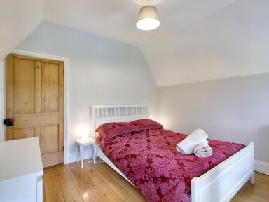A bedroom with a white bed with red patterned bedding wooden floor a wooden door and bedside table with lamp at Ingleside Adsett Royal Forest of Dean