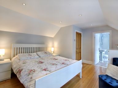 A bedroom with a bed with floral bedding two bedside tables with lamps a wooden floor and an open door leading to a bathroom at Ingleside Adsett Royal Forest of Dean