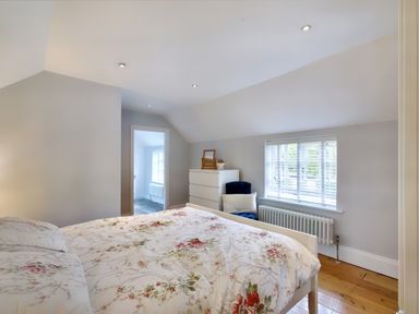 A bedroom with a floral bedspread a white chest of drawers a blue chair and a window with blinds at Ingleside in Adsett Royal Forest of Dean
