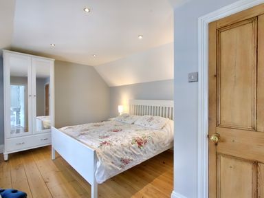 A bedroom with a white bed and floral bedspread a white wardrobe with mirrors a wooden door and wooden floor at Ingleside in Adsett Royal Forest of Dean