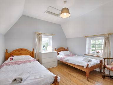 A bedroom with two single wooden beds white dresser between two windows and wooden chair at Ingleside Adsett Royal Forest of Dean