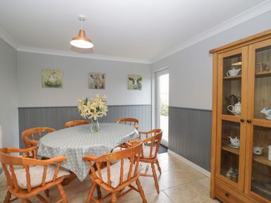 A dining room with a round table covered with a polka dot tablecloth surrounded by wooden chairs and a glass-front cabinet at Ingleside in Adsett Royal Forest of Dean
