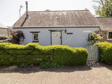 A white house with a grey tiled roof behind a trimmed green hedge and a wooden gate at The Old Stable in Wolfscastle near Haverfordwest