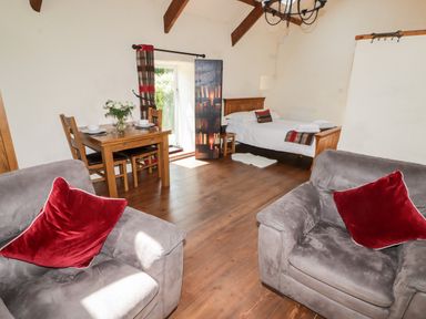 A living space with two armchairs with red cushions a wooden dining table with two chairs and a bed at The Old Stable in Wolfscastle near Haverfordwest
