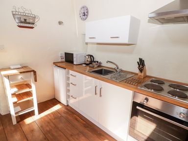 A kitchen with wooden floor white cabinets microwave kettle sink and stove at The Old Stable in Wolfscastle near Haverfordwest