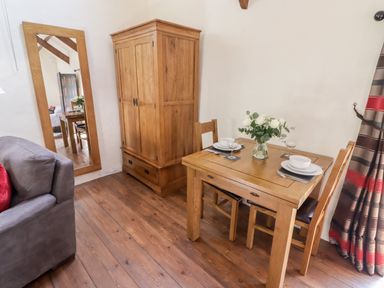 A dining area with a wooden table set for two next to a wooden wardrobe and a large wall mirror at The Old Stable in Wolfscastle near Haverfordwest