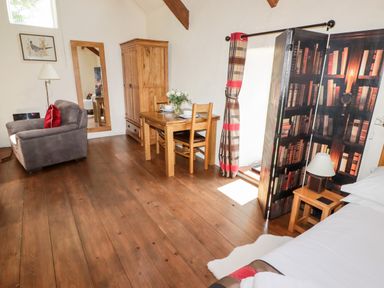A room with a wooden dining table and chairs a gray armchair a wooden wardrobe a mirror and a room divider with books image at The Old Stable in Wolfscastle near Haverfordwest