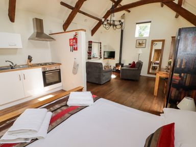 A room with a bed, kitchenette, two armchairs, a wood-burning stove, and wooden beams at The Old Stable in Wolfscastle near Haverfordwest