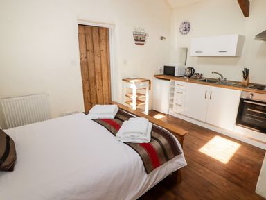 A bedroom with a bed towels and a kitchen area with white cabinets and wooden floor at The Old Stable in Wolfscastle near Haverfordwest
