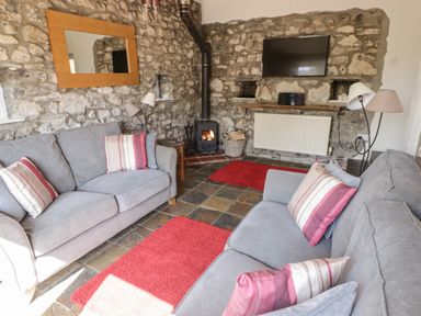 A living room with two gray sofas with striped cushions a wood burning stove a wall-mounted TV and stone walls at The Coach House in Wolfscastle