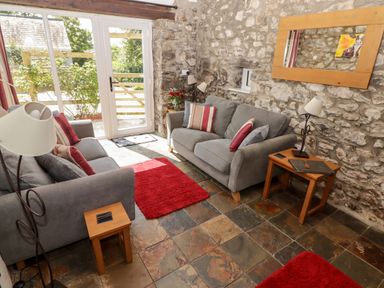 A sitting room with two gray sofas red cushions wooden side tables and stone walls at The Coach House in Wolfscastle