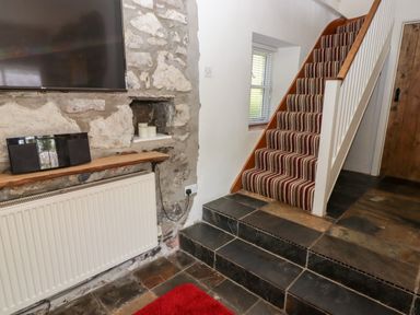 A staircase with striped carpet next to a stone wall with a mounted television and a radiator at The Coach House in Wolfscastle