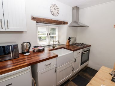 A kitchen with wooden countertops a white sink an electric stove a microwave kettle and a window above the sink at The Coach House in Wolfscastle