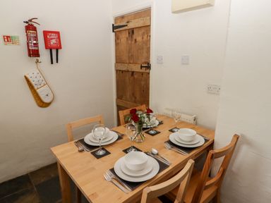 A dining room with a wooden table set for four with plates glasses and cutlery and a wooden door at The Coach House in Wolfscastle