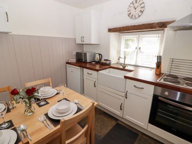 A kitchen with a wooden dining table set with plates and glasses a bouquet of red roses a sink stove oven microwave kettle and knives at The Coach House in Wolfscastle