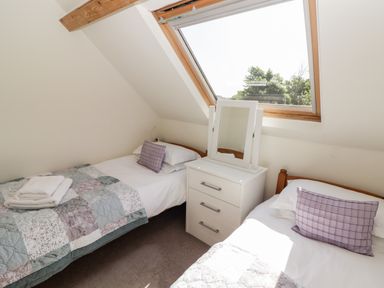 A bedroom with two single beds a white dresser with a mirror and a skylight window showing trees at The Coach House in Wolfscastle