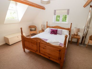 A bedroom with a wooden bed white bedding two bedside tables with lamps a wicker chair and two windows at The Coach House in Wolfscastle