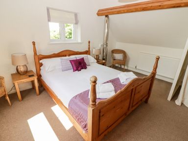 A bedroom with a wooden double bed bedside tables with lamps two wicker chairs and a small window at The Coach House in Wolfscastle