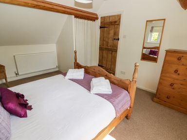 A bedroom with a wooden bed with pillows and towels a wooden dresser a mirror and a wooden door at The Coach House in Wolfscastle