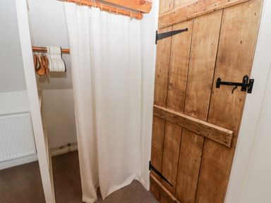 A closet space with a wooden door a hanging rod with wooden hangers and a white curtain covering part of the closet at The Coach House in Wolfscastle