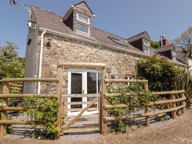 Exterior of a stone house with wooden fence and gate under clear sky at The Coach House in Wolfscastle