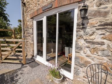 Exterior view of a stone building with glass patio doors wooden gate and potted flowers at The Coach House in Wolfscastle