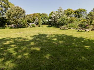 A grassy garden area with picnic benches and a football goal surrounded by trees at The Coach House in Wolfscastle