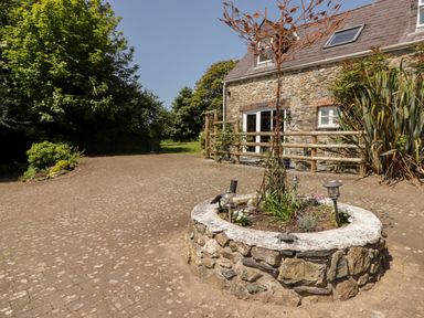 A stone planter with plants on a paved area in front of a stone house with trees in the background at The Coach House in Wolfscastle