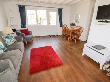 A living room with a sofa and armchair near a red rug and a dining table with chairs at The Duck House in Wolfscastle