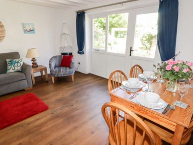 A dining area with a wooden table set for four and a living area with chairs and a sofa near glass doors at The Duck House in Wolfscastle