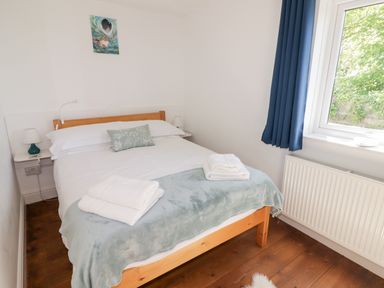 A bedroom with a wooden bed white bedding folded towels a bedside lamp and a window with blue curtains at The Duck House in Wolfscastle