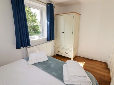 A bedroom with a bed, folded towels, a window with blue curtains, and a cream wardrobe at The Duck House in Wolfscastle