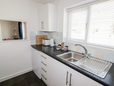 A kitchen counter with a sink a dish rack a toaster a kettle and a window with blinds at The Duck House in Wolfscastle
