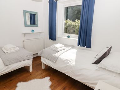 A bedroom with two single beds with grey blankets and white towels on wooden floor with white walls and a window with blue curtains at The Duck House in Wolfscastle