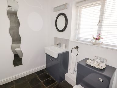 A bathroom with a sink vanity unit a round mirror a wavy full-length mirror and a window with blinds at The Duck House in Wolfscastle