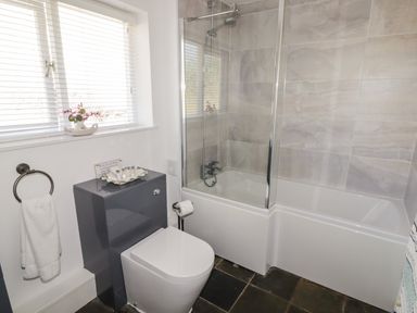 A bathroom with a toilet sink bathtub with glass shower screen and a window with blinds at The Duck House in Wolfscastle