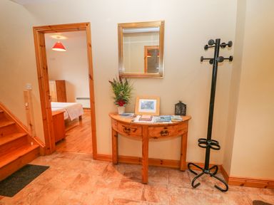 An entryway with wooden stairs a wooden console table with items on it a mirror above and a black coat rack at Mary Agnes Cottage in Cahirkeen near Allihies County Cork